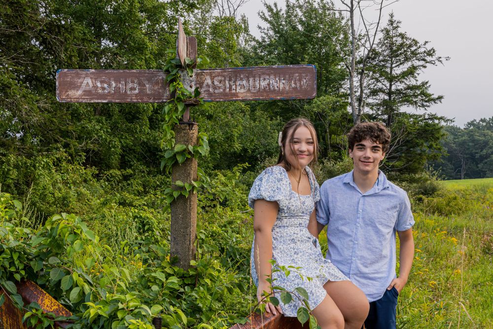A couple poses together on a nature trail surrounded by lush summer greenery.