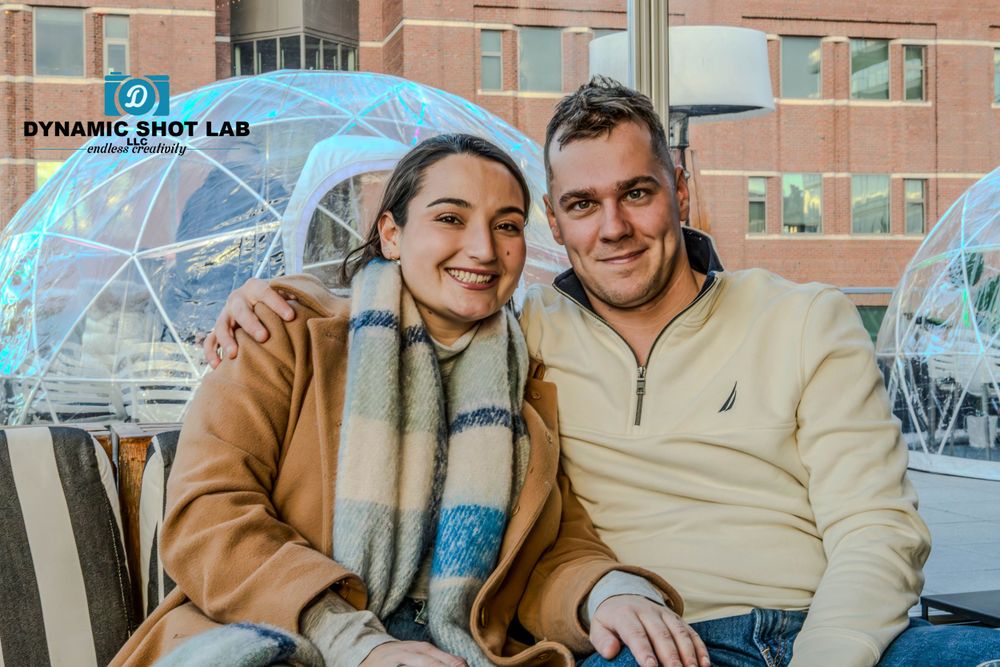 A couple sits together in a cozy outdoor dining dome during winter.