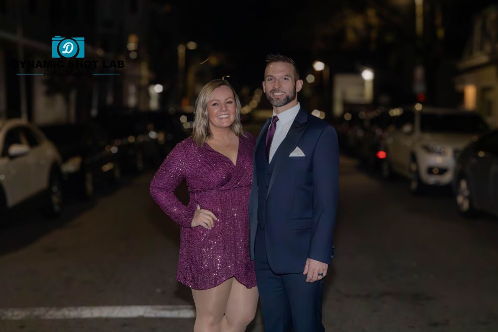 A couple poses together on a city street at night for a formal portrait.