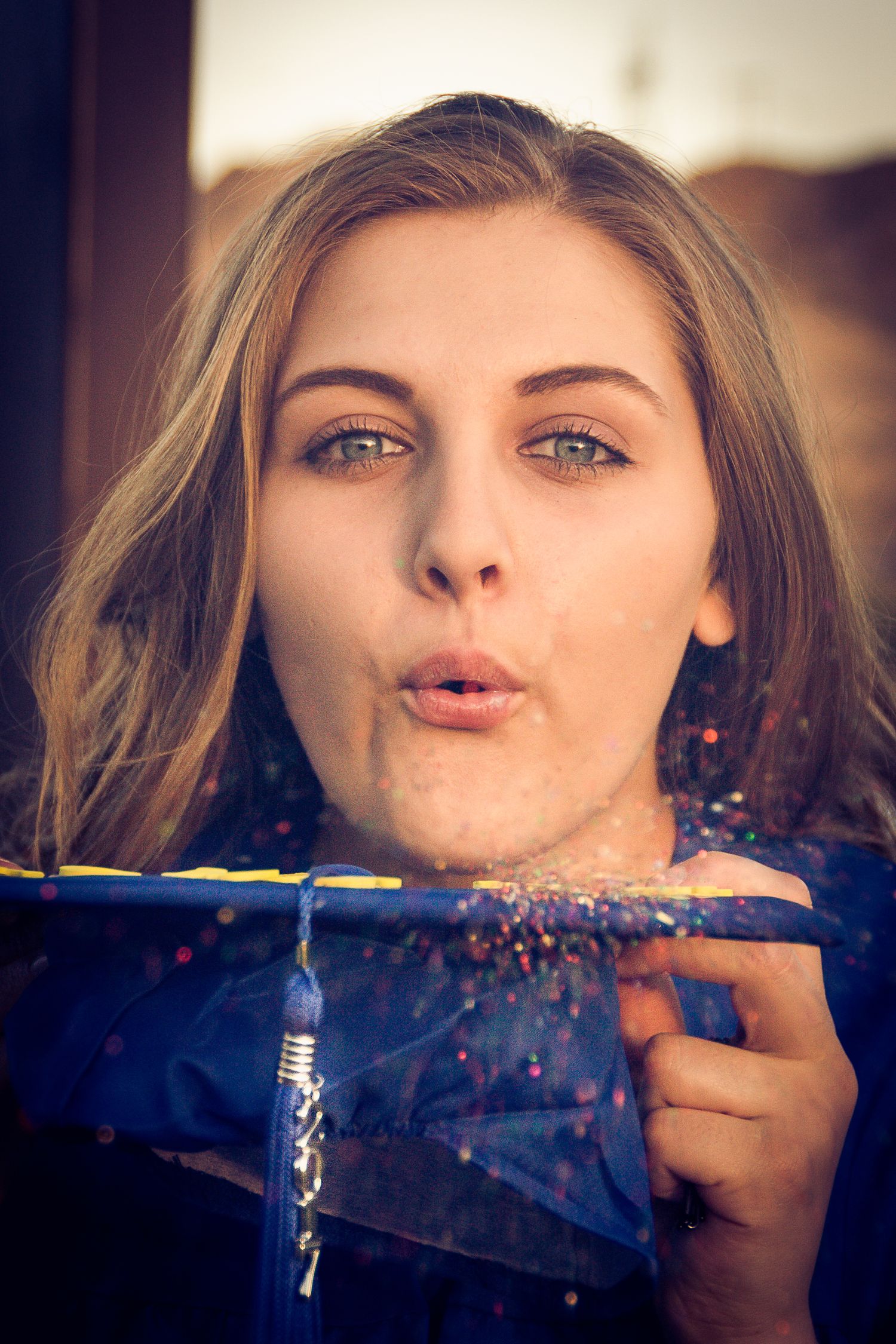 Photo showing someone blowing glitter off of graduation cap.