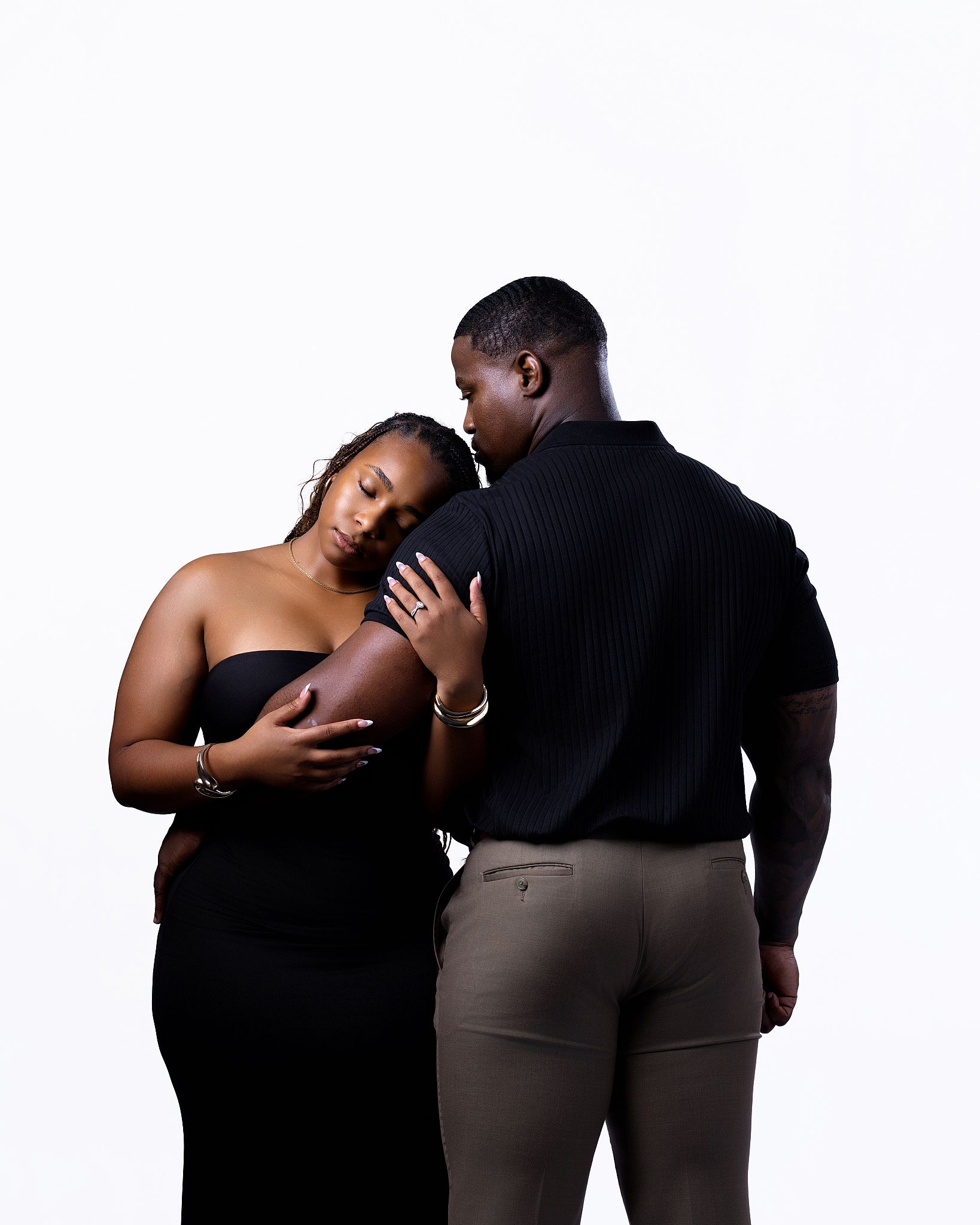 A pregnant couple in matching black outfits poses tenderly against a white background in a maternity photo shoot.