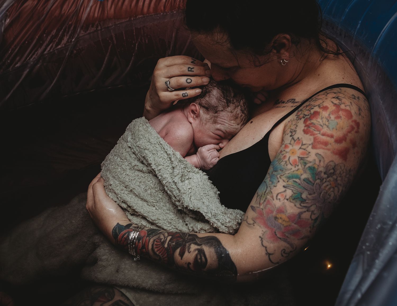 Tender nighttime moment with tattoo-adorned parent and sleeping infant.