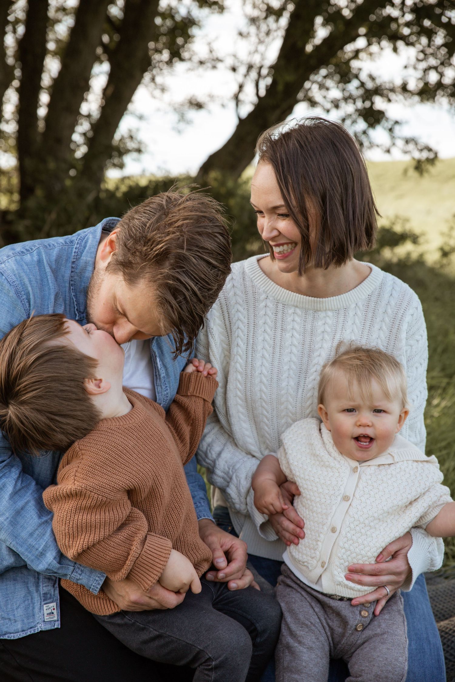 Joyful family moment captured outdoors with casual sweaters and genuine laughter.