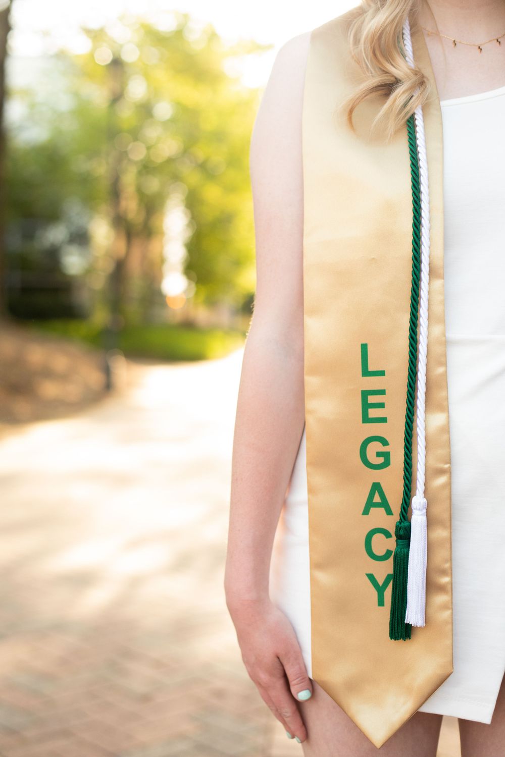 Close-up detail of gold graduation stole with green lettering against white dress.