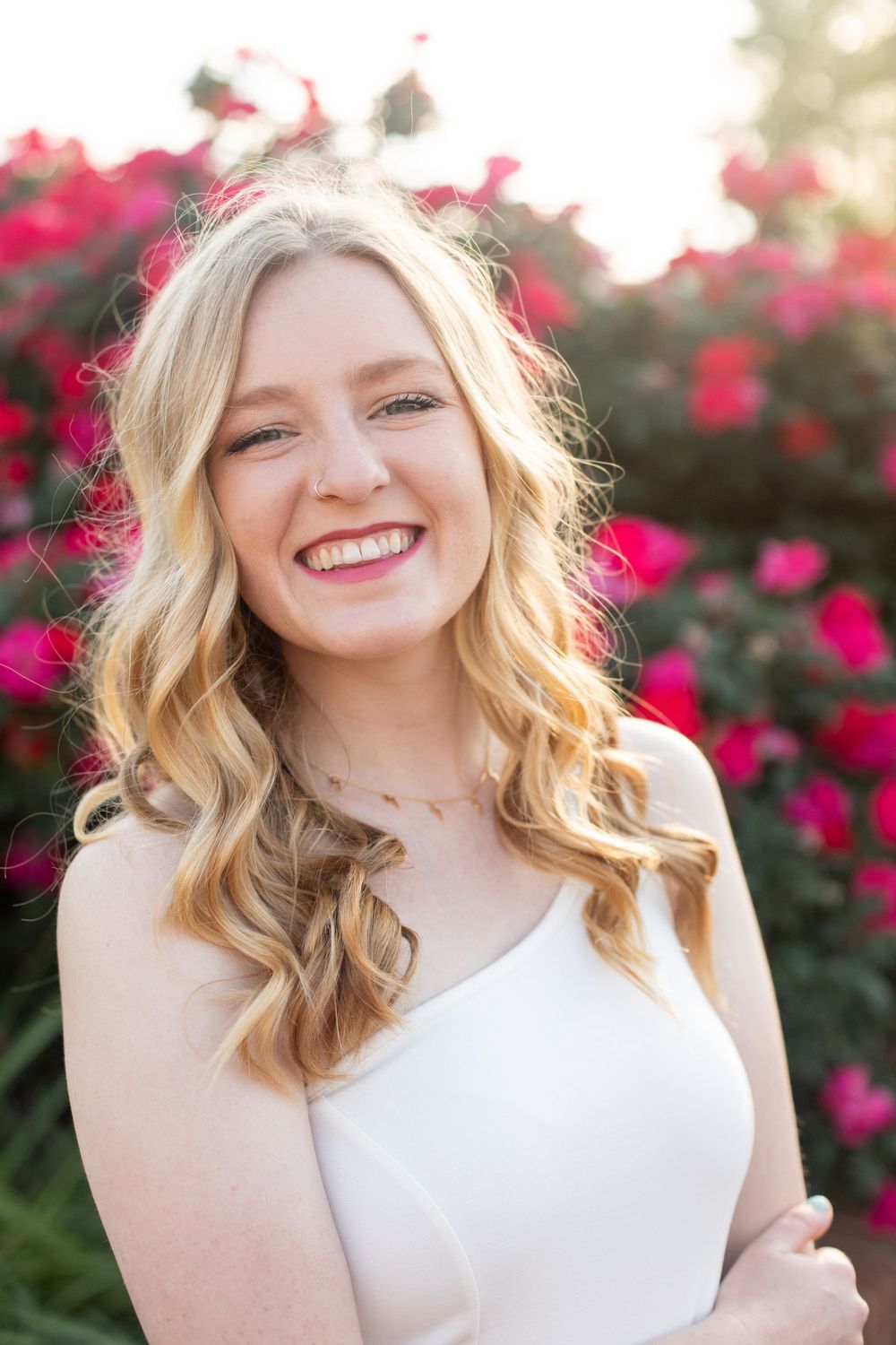 Portrait of graduate in white dress with red floral backdrop during sunset.