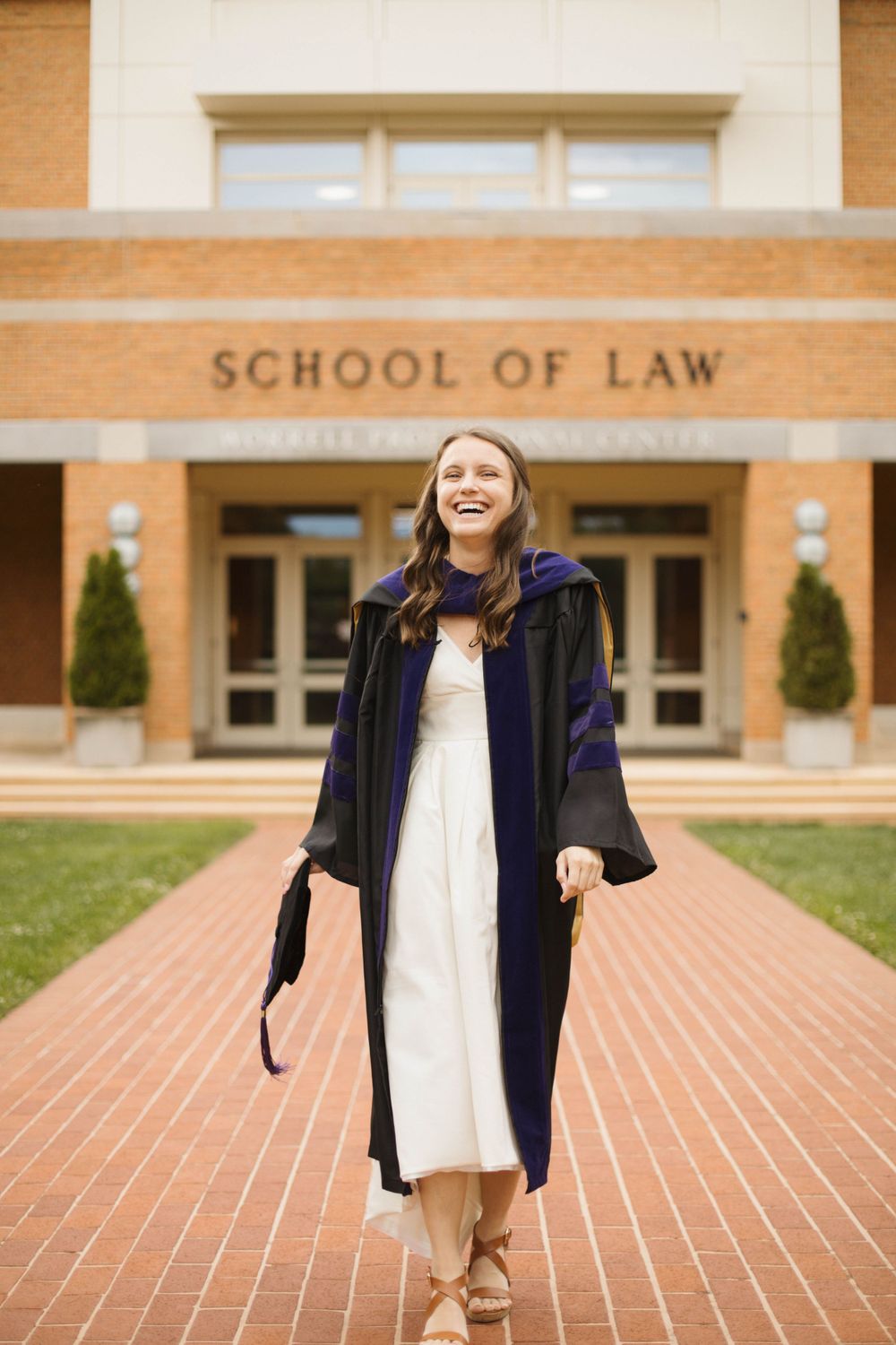 Graduate in academic regalia jumping joyfully outside School of Law entrance.
