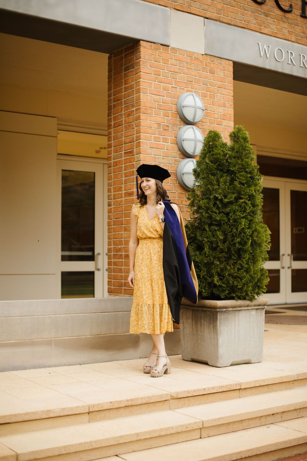 Series of poses in yellow dress and graduation gown outside brick law school building.