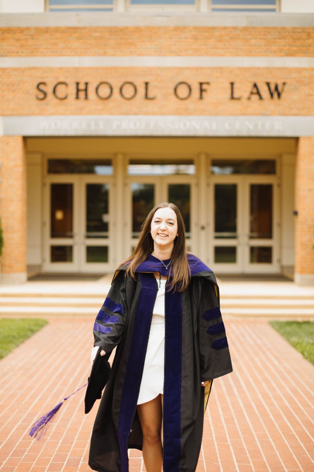 Graduate in academic regalia jumping joyfully outside law school entrance.
