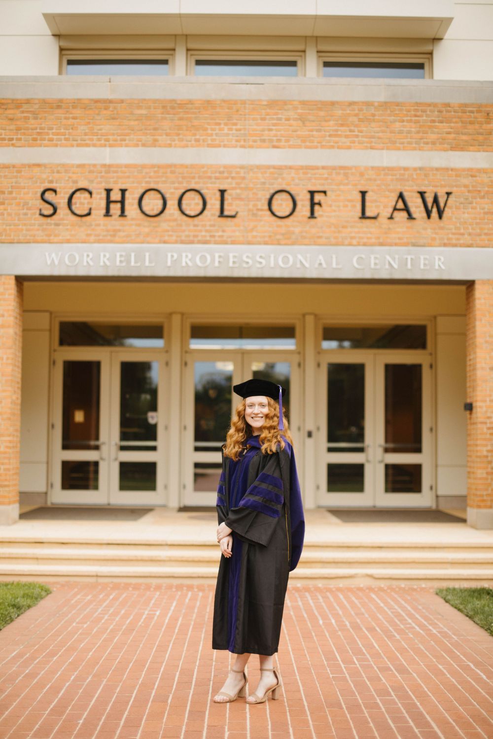 Graduate in academic regalia posing in front of law school entrance.