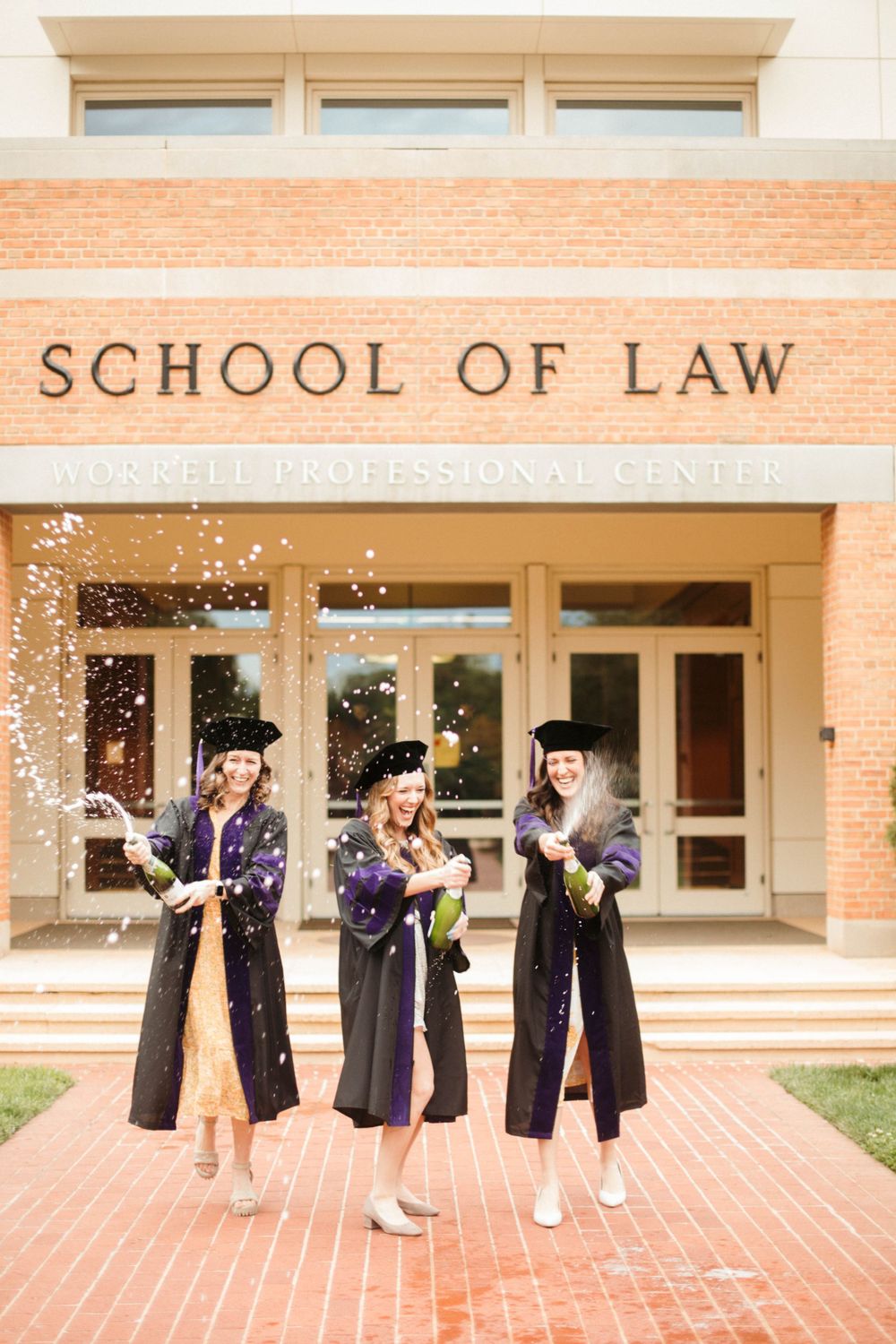 Law school graduates celebrating with confetti outside brick building entrance.