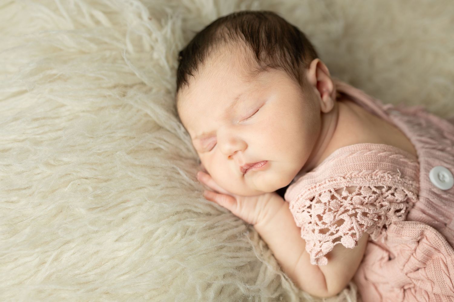 Sleeping newborn wrapped in brown fabric on soft fur blanket with green foliage accents.