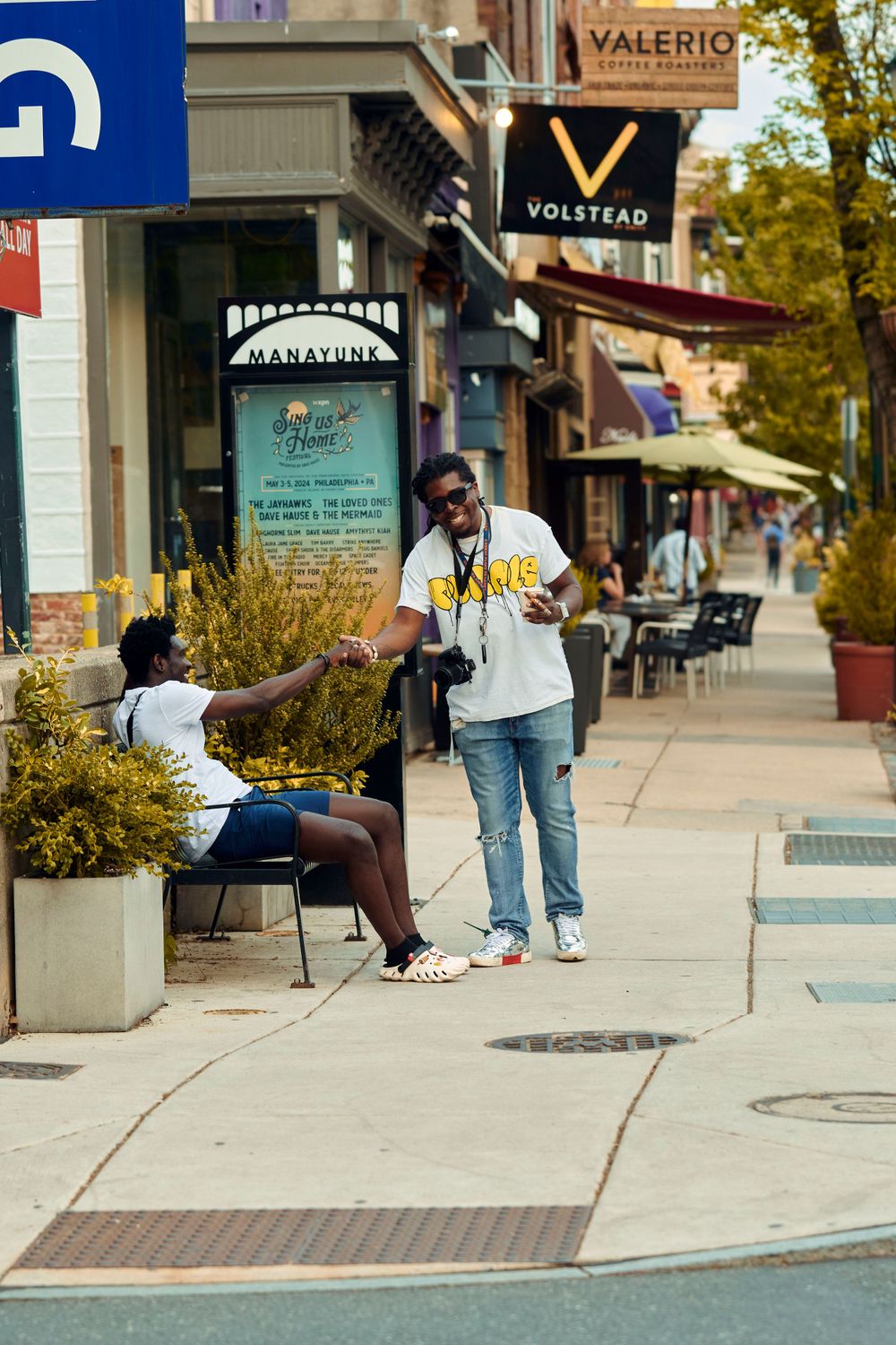 People walking on a sidewalk past storefronts with signs for Valerio and Voltstar.