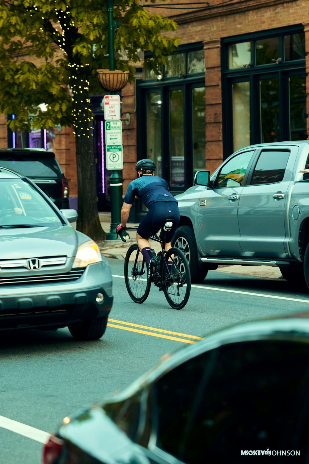Urban street scene with parked cars and cyclists on a brick-lined street.