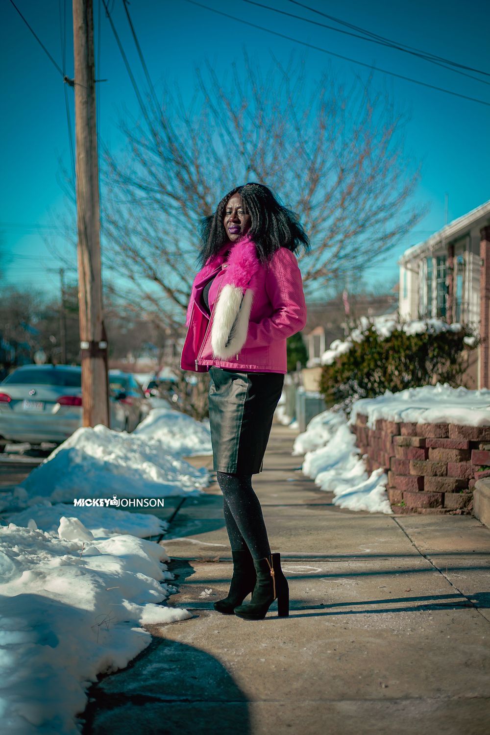 Winter fashion shoot featuring boots and pink jacket against snowy urban backdrop.
