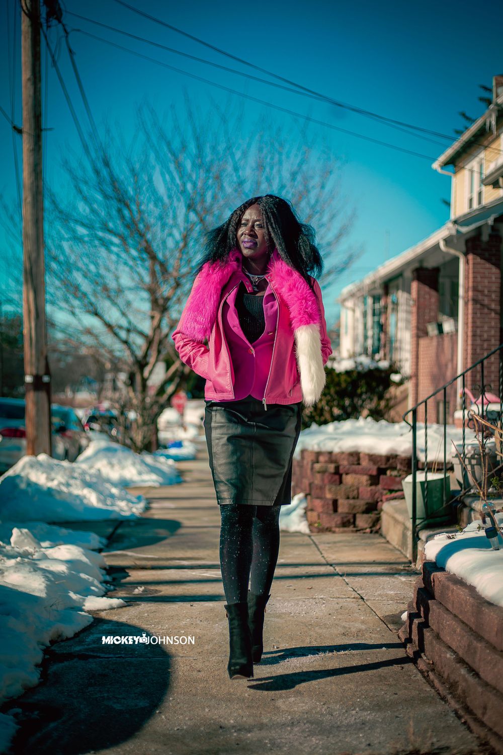 Person walking on snowy sidewalk wearing vibrant pink coat.