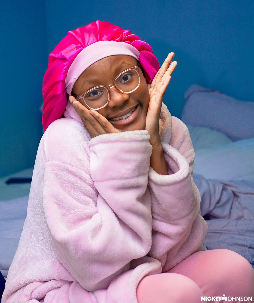 Cozy indoor portrait wearing pink hat and light sweater against blue background.