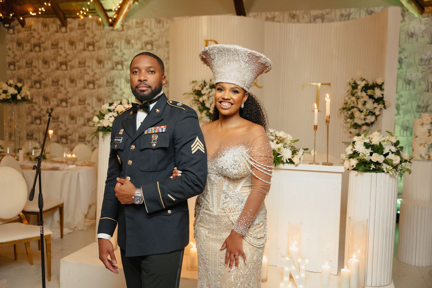 Wedding couple posing in formal attire against floral decorated indoor backdrop.