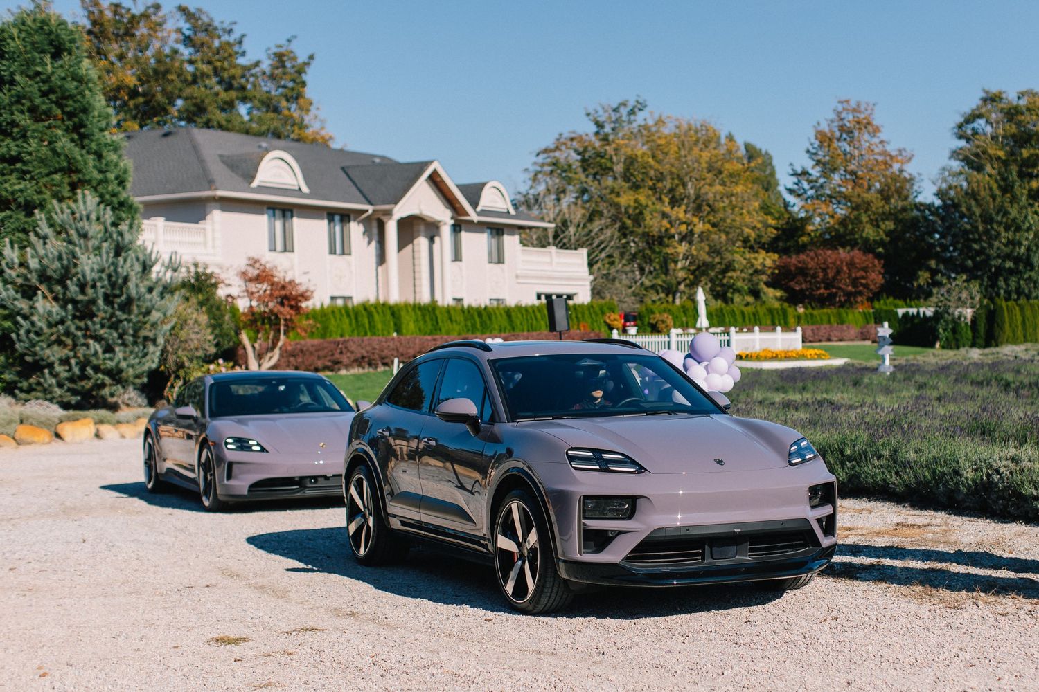 Two Porsche electric vehicles parked in front of suburban houses on a sunny day.