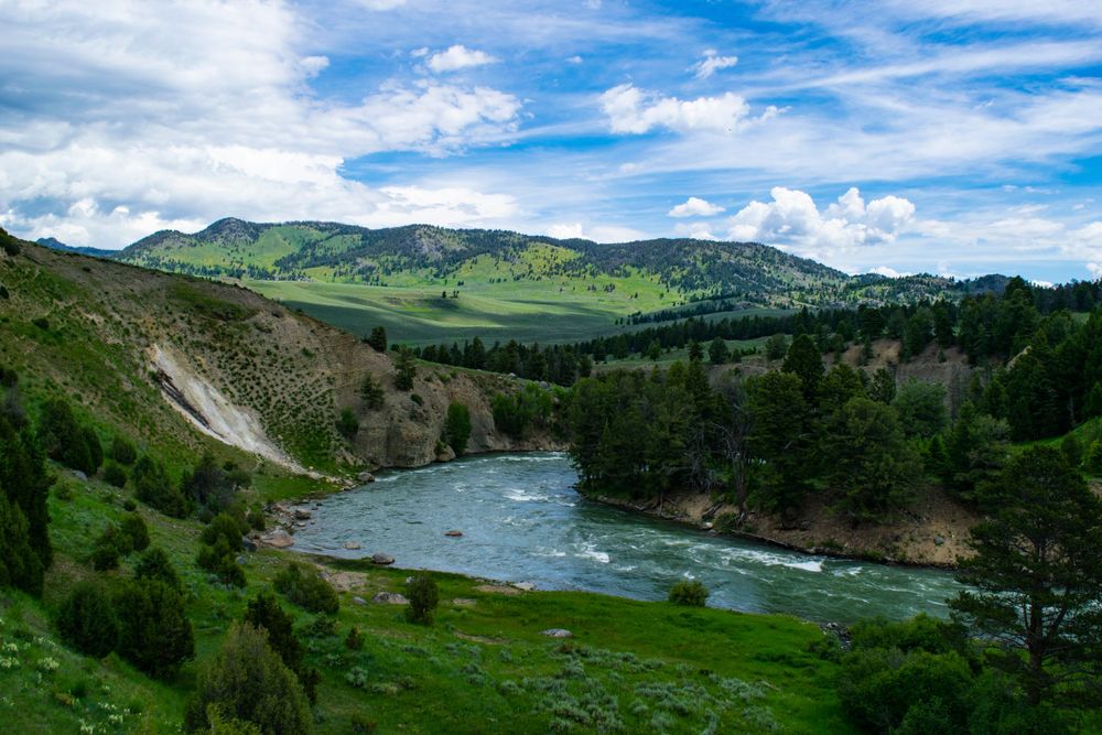 Winding river cuts through green mountain valley under dramatic blue sky.