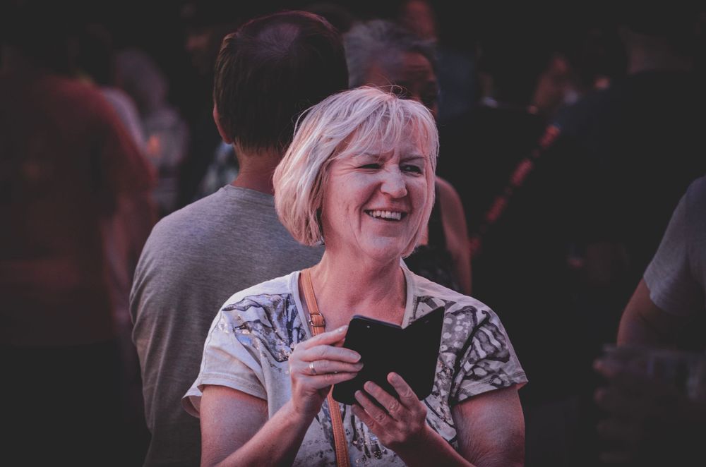 Someone joyfully looking at a mobile phone screen while laughing outdoors.