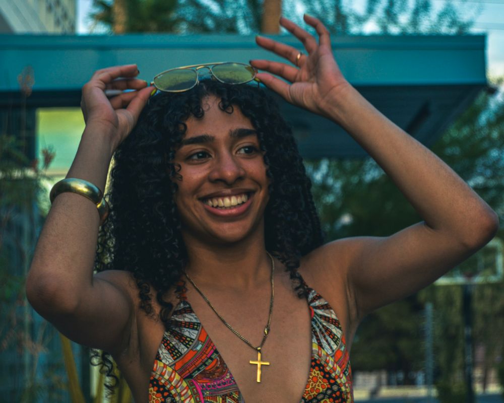 Person in floral dress dancing joyfully outdoors on a sunny day.