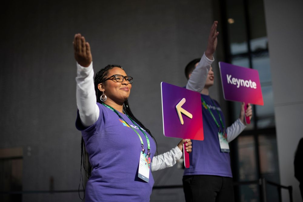 Event participant in purple vest raising arms enthusiastically during presentation.