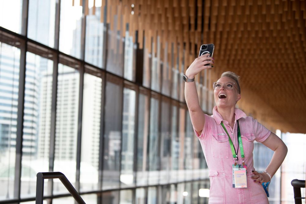 Professional taking selfie in modern office corridor with wooden ceiling details.