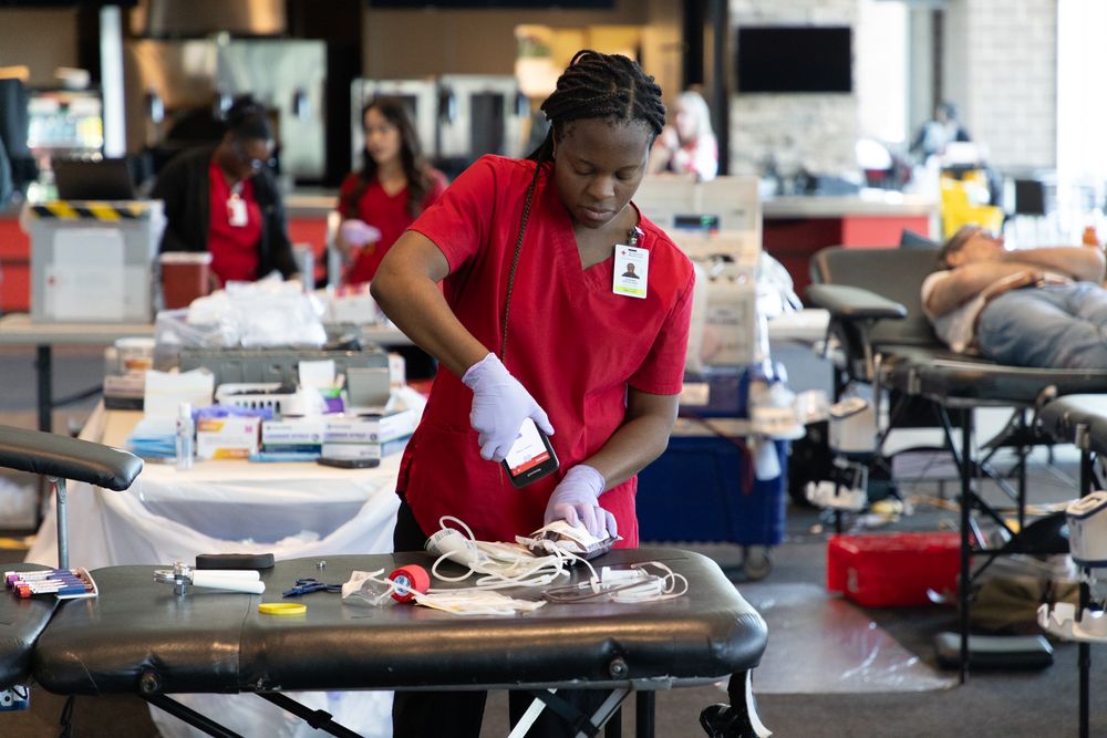 Healthcare workers wearing red scrubs draw blood samples from donors at a blood donation center.