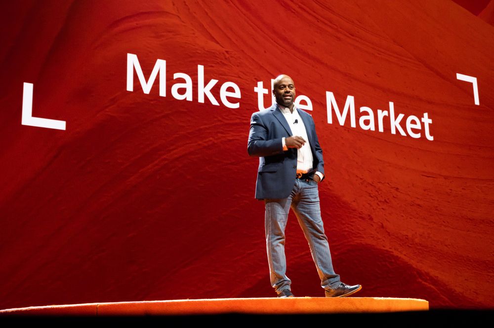 Speaker presenting in front of red wall with 'Make the Market' text display.
