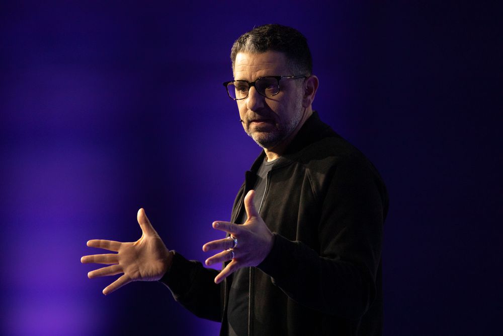 Speaker gestures passionately while giving presentation with purple lighting effects.