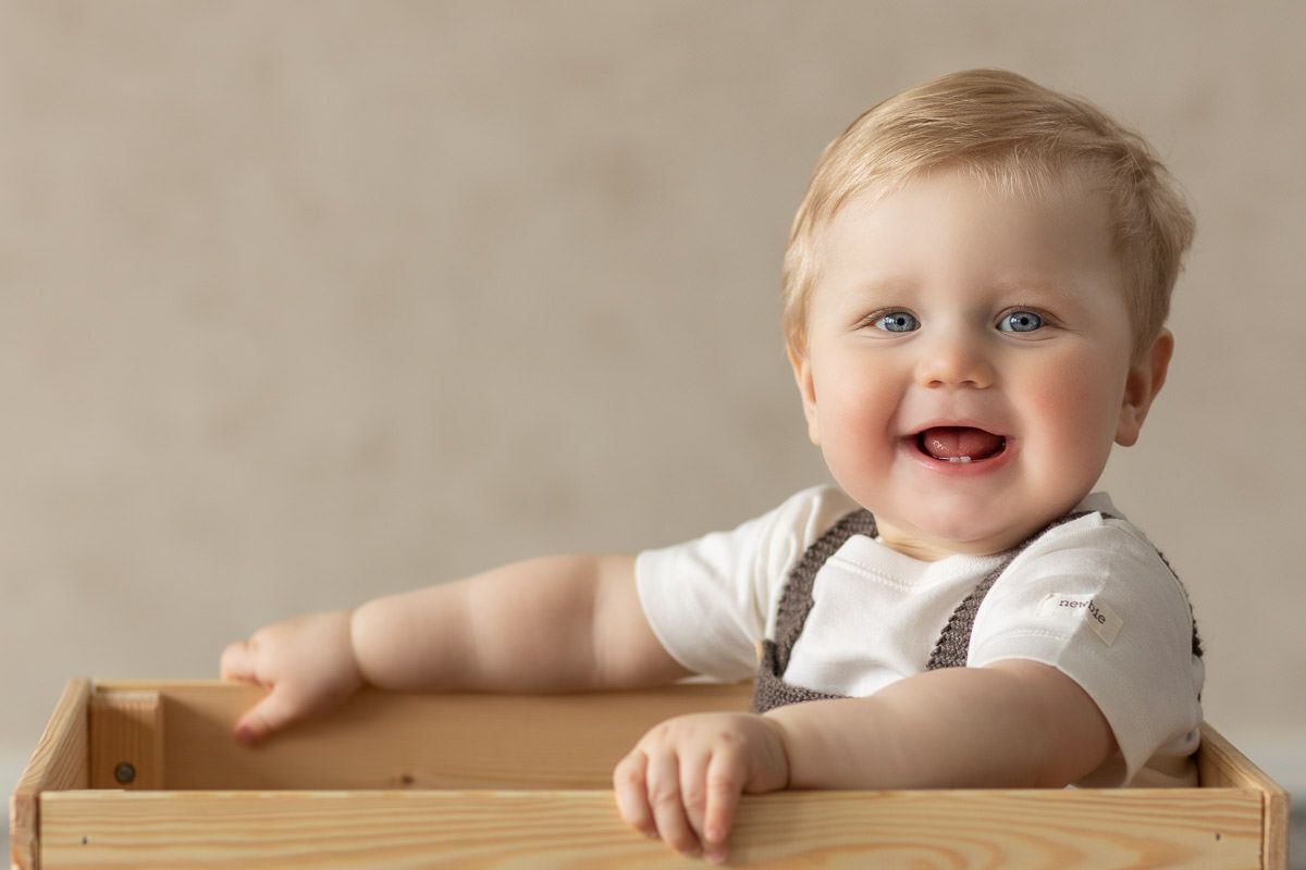 Ettårsfotografering av gutt. Han sitter i en trekasse og smiler til kamera.