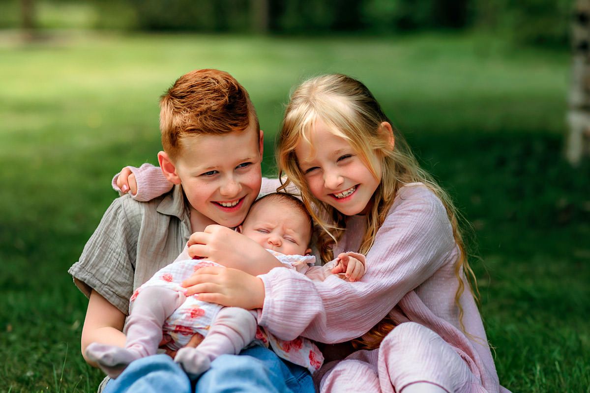 Storebror og lillesøster holder nyfødt lillesøster mens de ler sammen. Tatt av familiefotograf Tone Ørstavik i Rogaland Arboret.