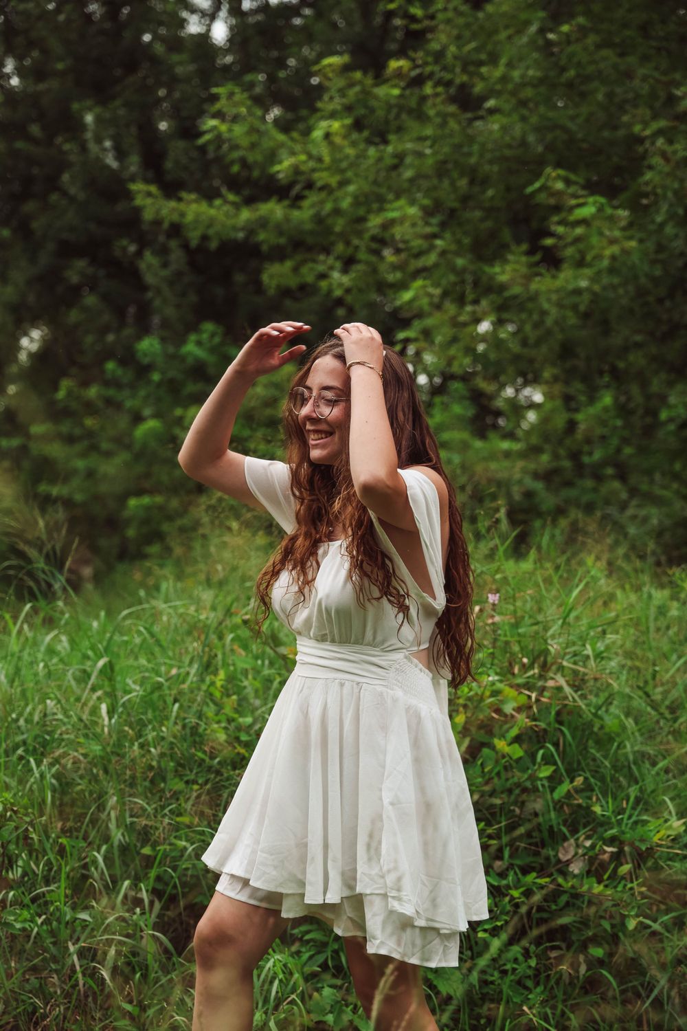Carefree dancing in white dress among green summer foliage.