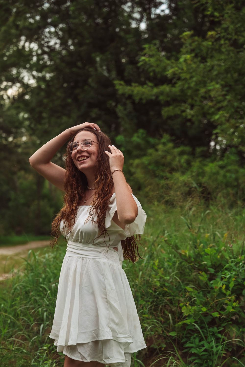 Joyful moment captured in white dress against lush forest backdrop.
