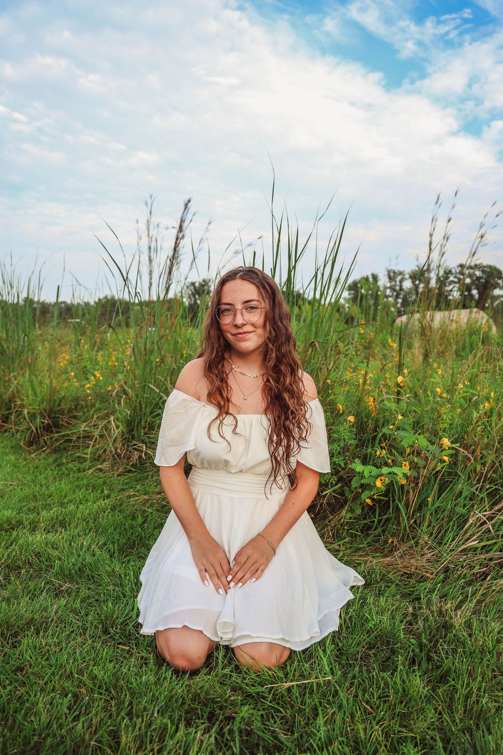 A dreamy outdoor portrait in a meadow with tall grass and wildflowers featuring a white summer dress.