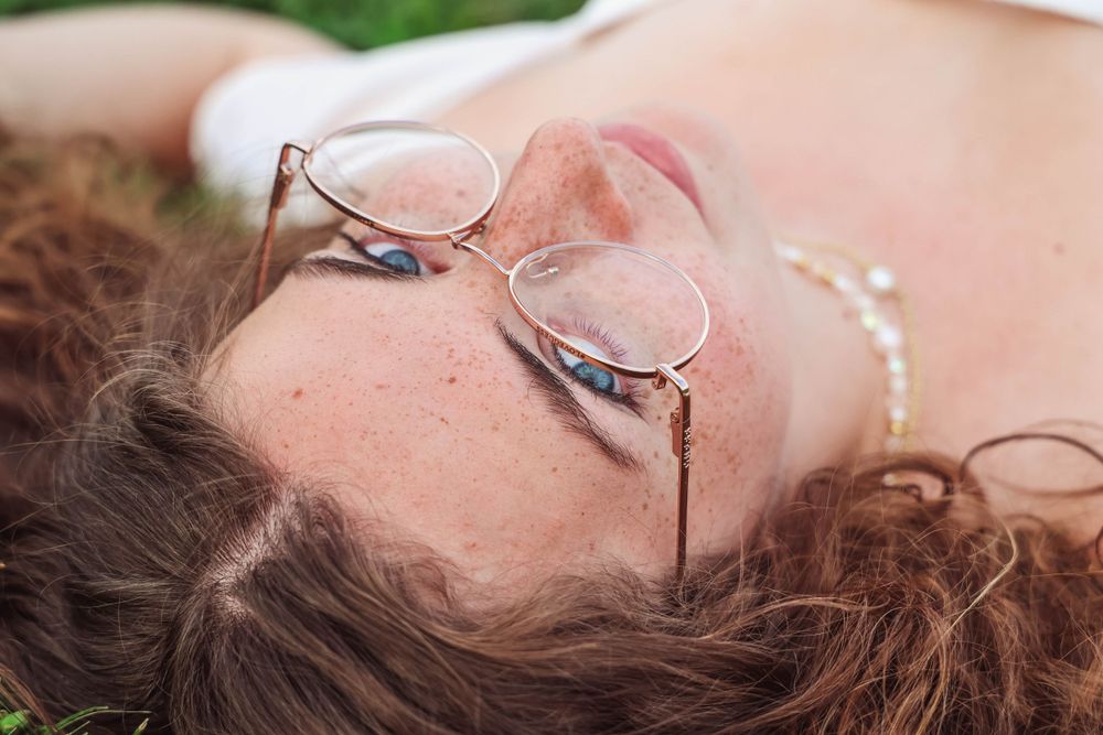 Close-up detail shot of round glasses and wavy hair against a soft natural background.