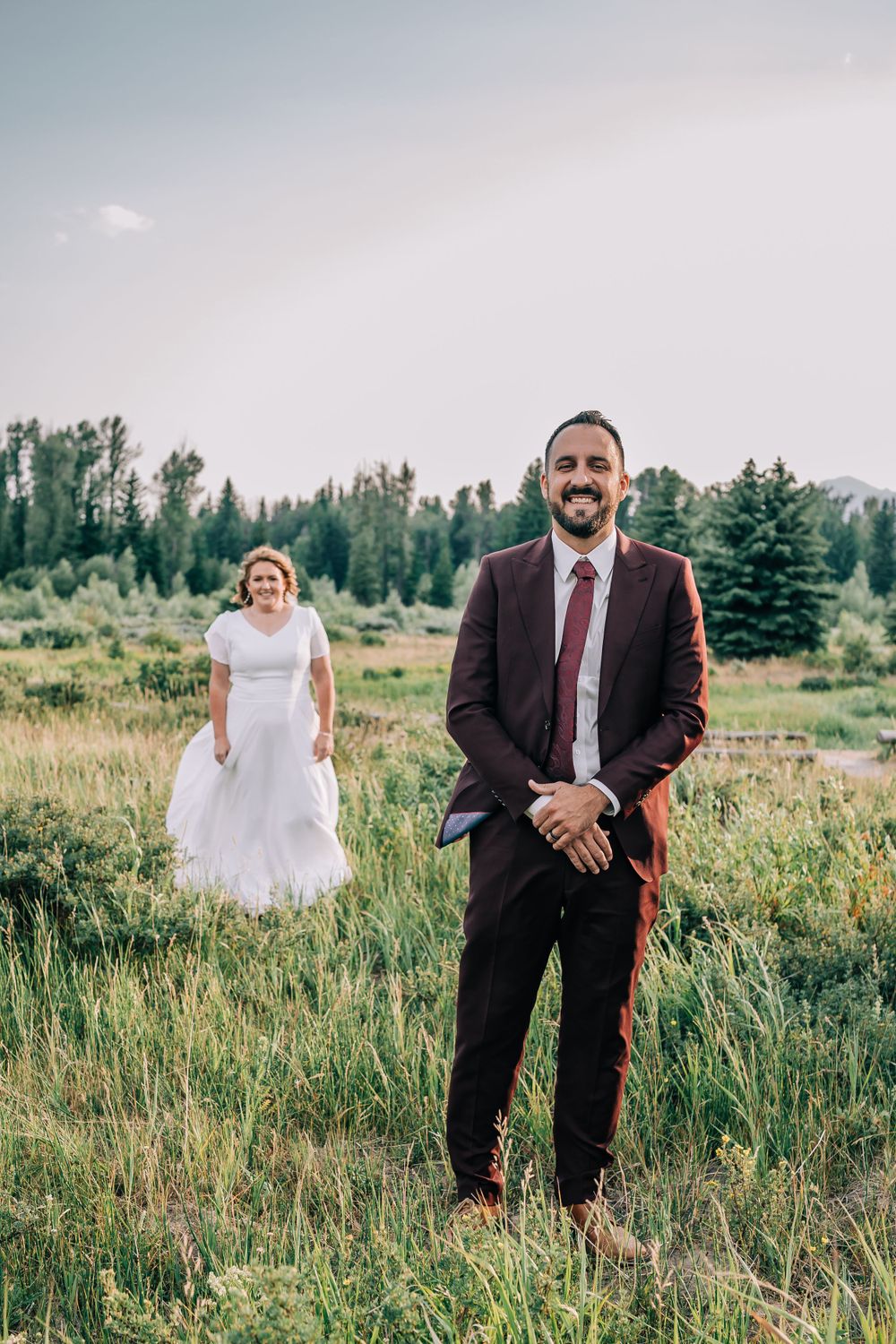 Groom smiles waiting patiently for first look of his bride in a mountain field