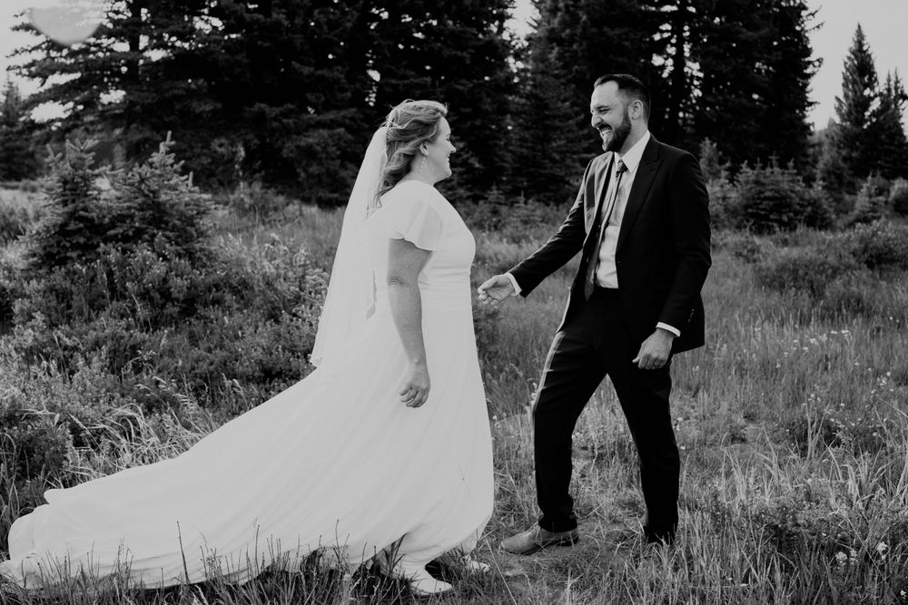 Black and white image of the bride and groom walking hand in hand through a field in the Teton mountains
