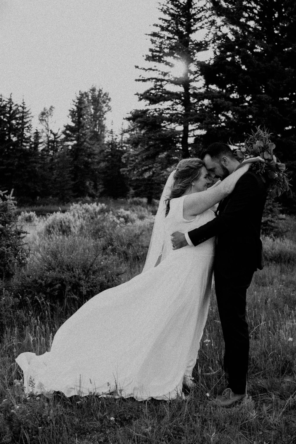Black and white image of bride and groom in a tender embrace in the Teton Mountain field