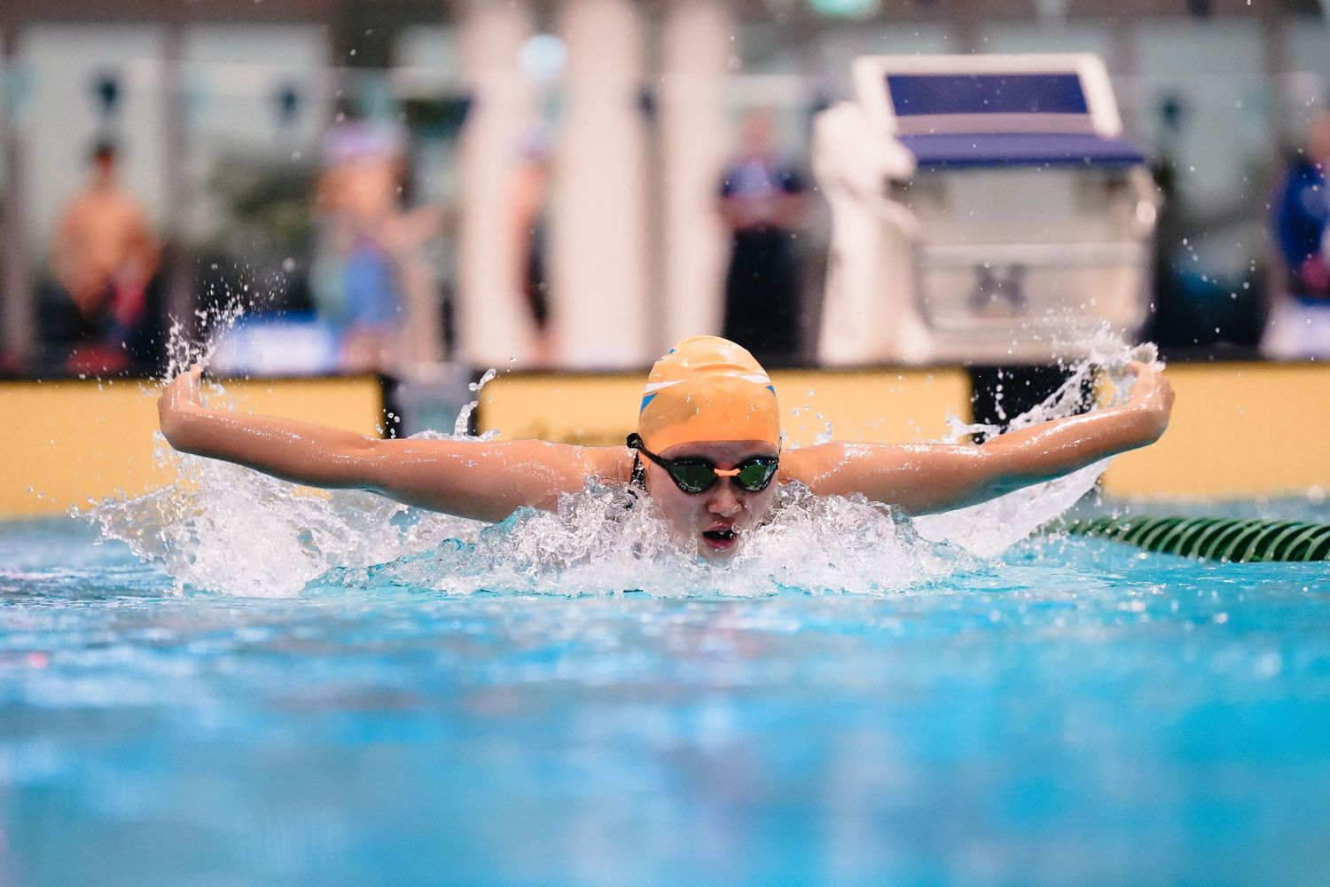 Swimmer performing butterfly stroke with water splashing during competition.