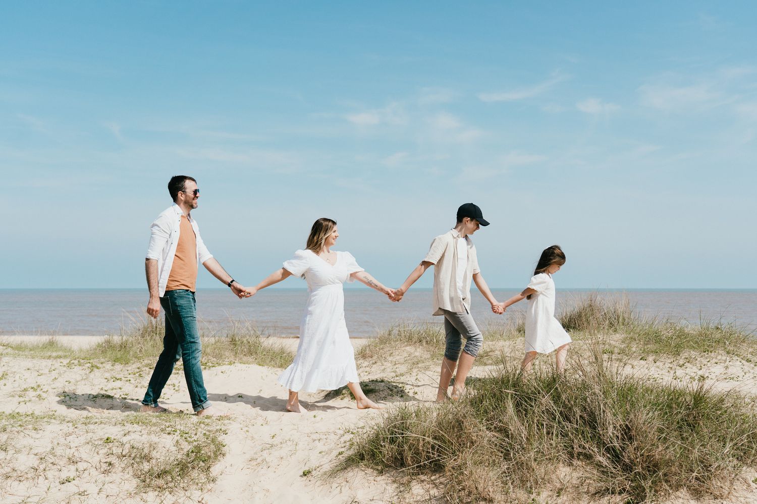 Family walking in line holding hands along coastal beach path.