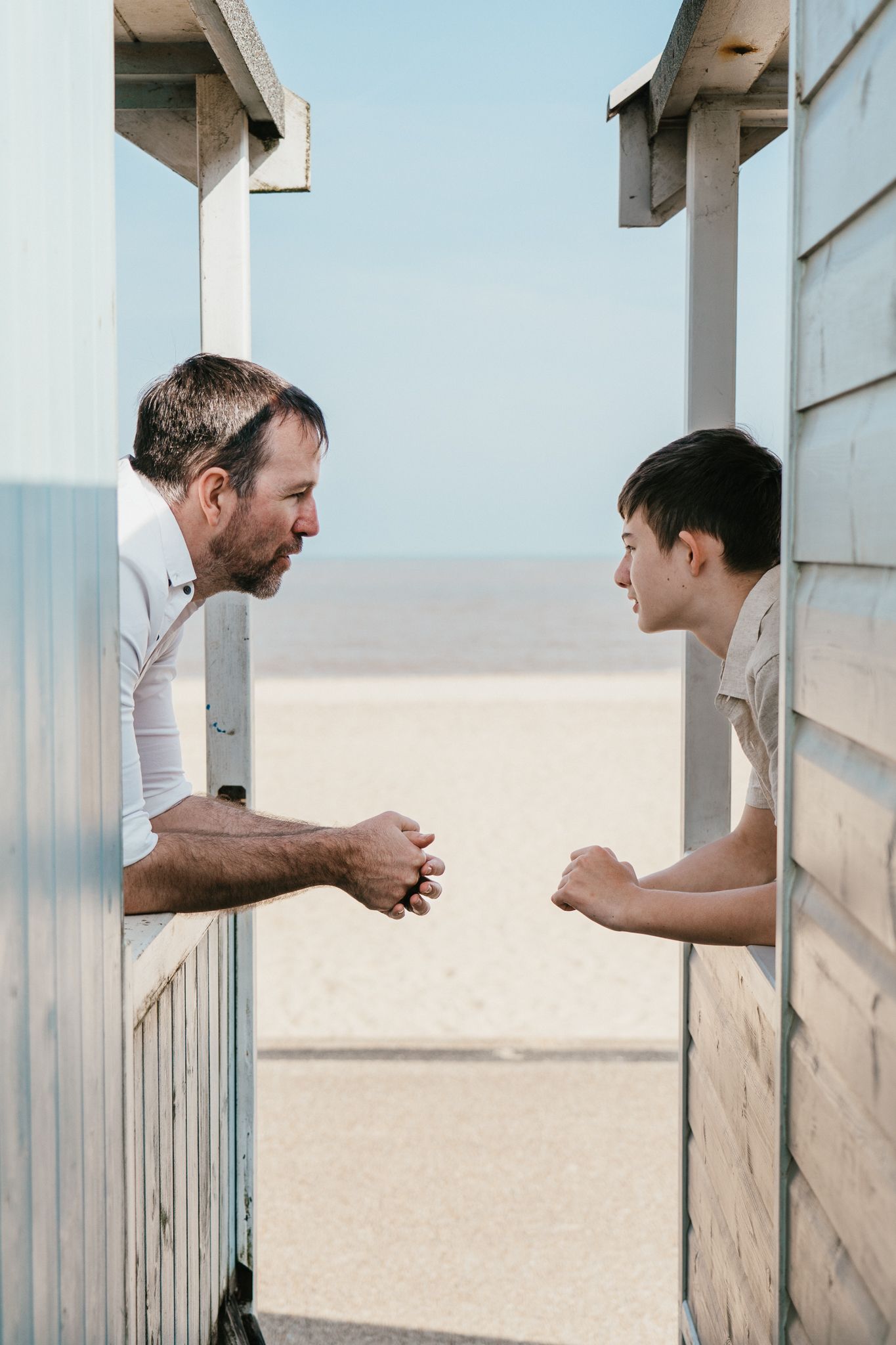 Dad and son having a playful conversation between beach hut walls.