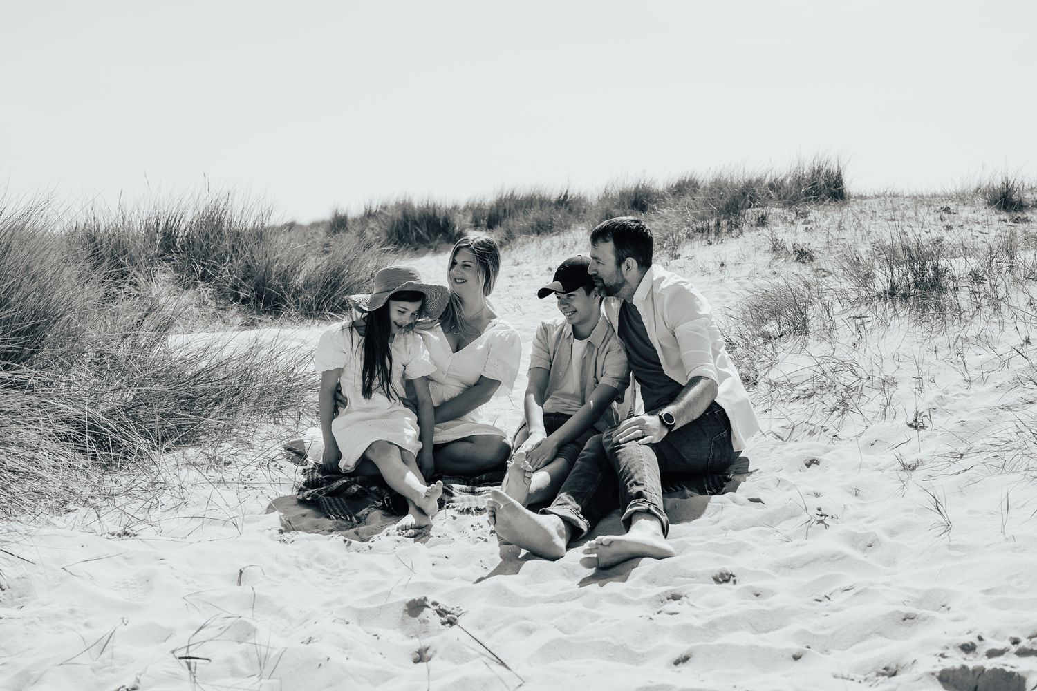 Family sitting together on sandy beach dunes in black and white.