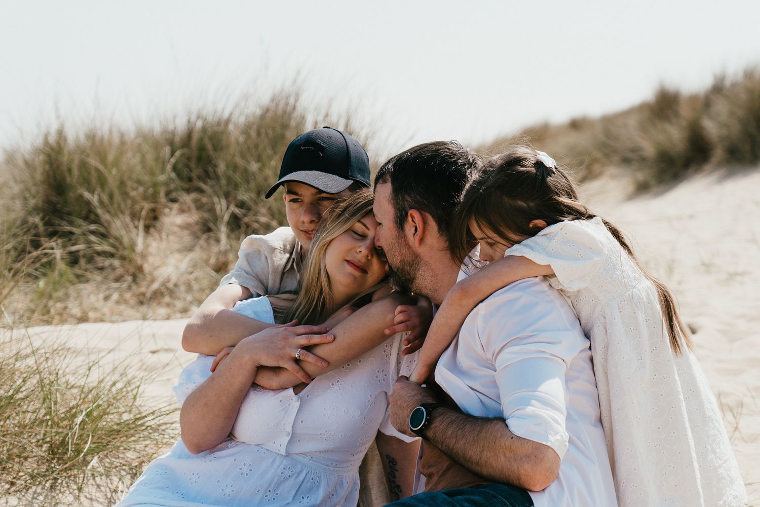 Family sharing intimate moment on beach dunes.