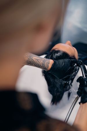 Close-up van de getatoeëerde handen van een haarstylist die aan het haar van een klant werkt in de salon.