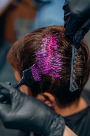 Haarkleursessie waarbij felroze verf wordt aangebracht met zwart gehandschoende handen.