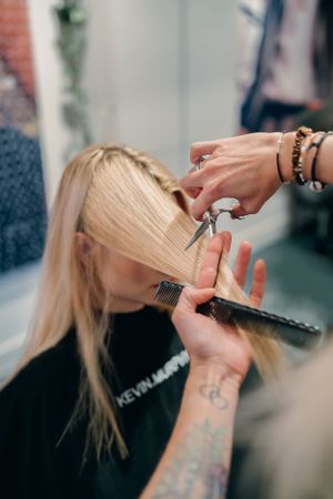 Professionele haarstylist met tatoeages die blond haar bijwerkt met een schaar.