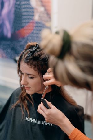 Haarstylist aan het werk aan het haar van een klant, terwijl ze een Kevin Murphy saloncape draagt.