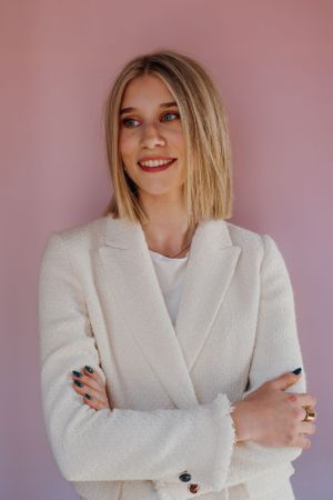 Professionele headshot van een model in een crèmekleurige blazer tegen een roze achtergrond.