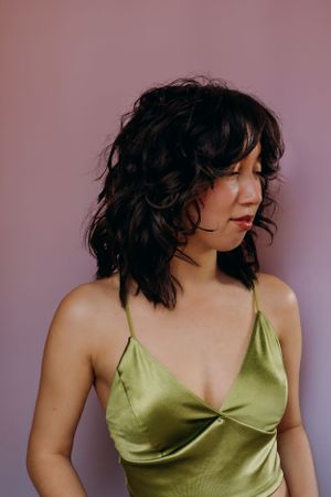 Portret van een model in een zijden groene camisole tegen een roze achtergrond met dramatisch licht.